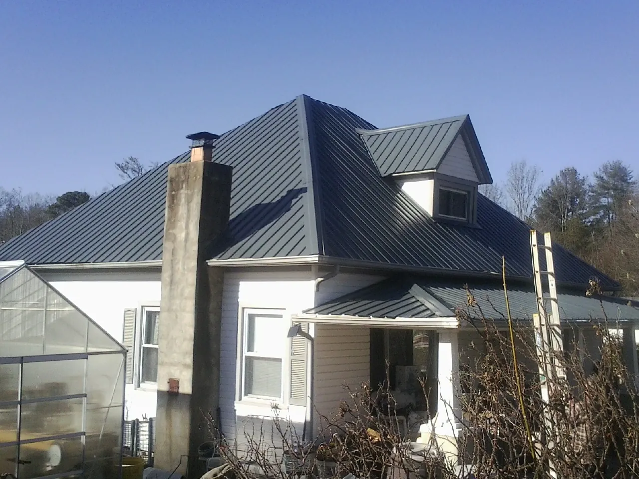 Dark blue standing seam metal roof on a white farmhouse with dormer — Slate & Tile Roof Repair by Roofing Brothers in Calimesa