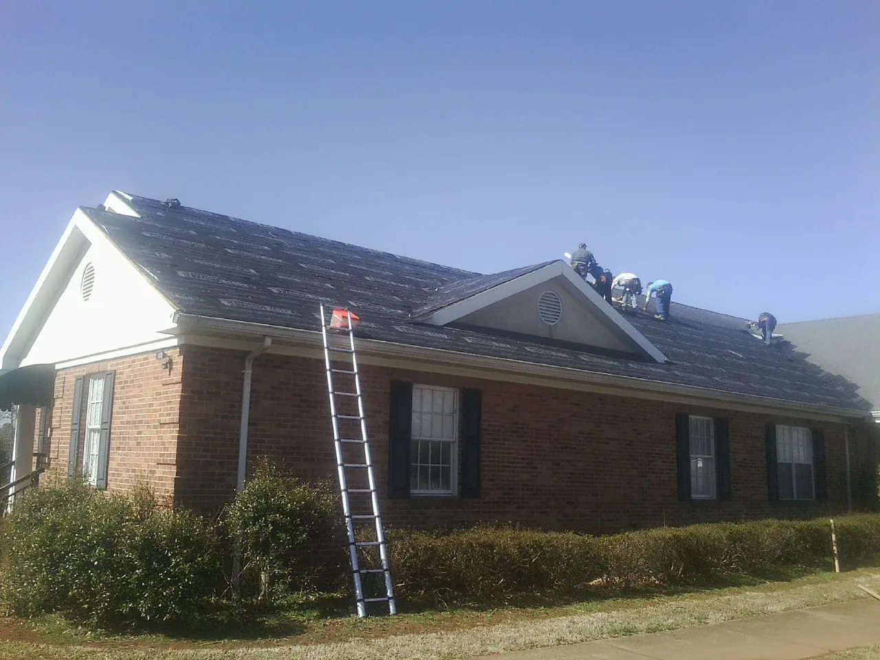 Crew tearing shingles off a brick ranch roof with a ladder set — Emergency Roof Repair work by our crew in Calimesa