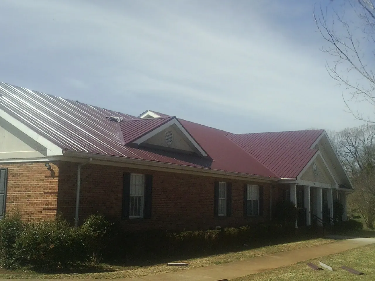 Red metal roof with gabled entries on a long brick building, from a Hail Damage Roof Repair job in Calimesa