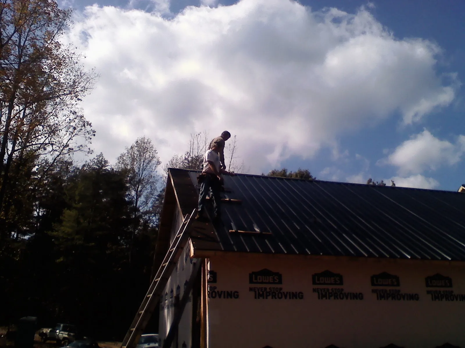 Roofer fastening dark metal panels high against a cloudy sky, from a Roof Inspection job in Calimesa