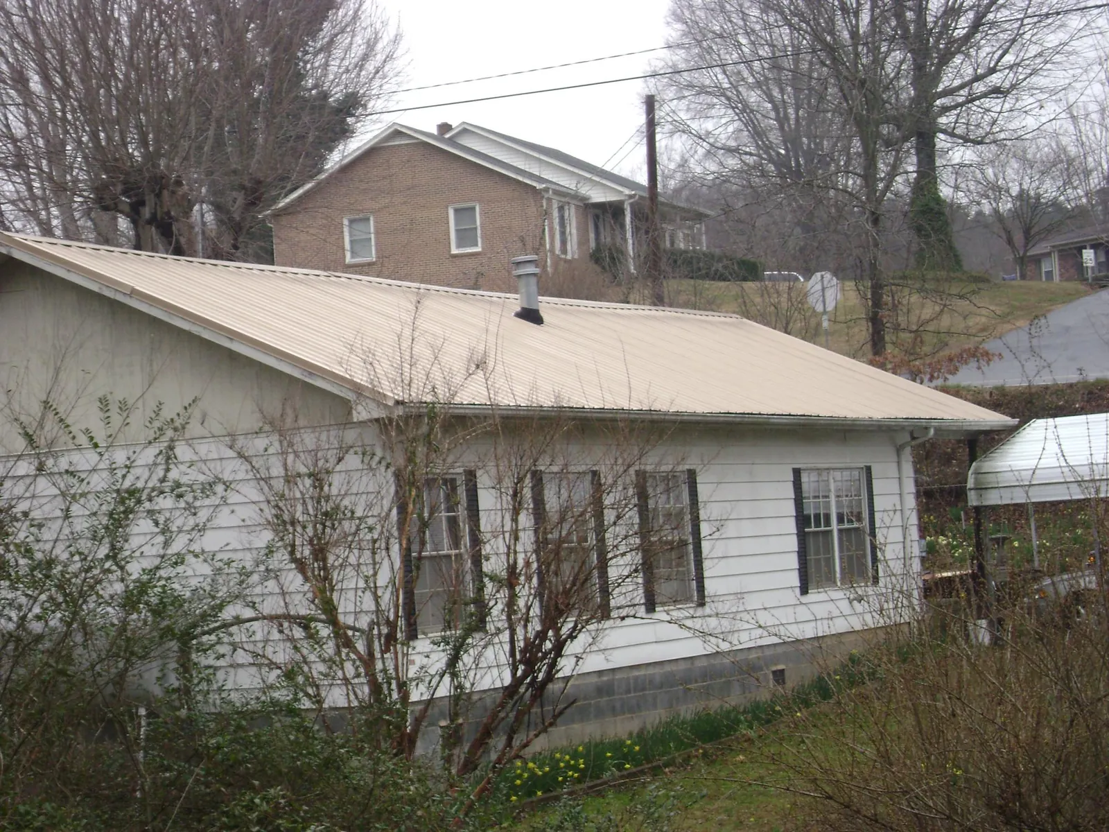 Tan metal roof on a white sided house set into a hillside — Commercial Roofing by Roofing Brothers in Calimesa